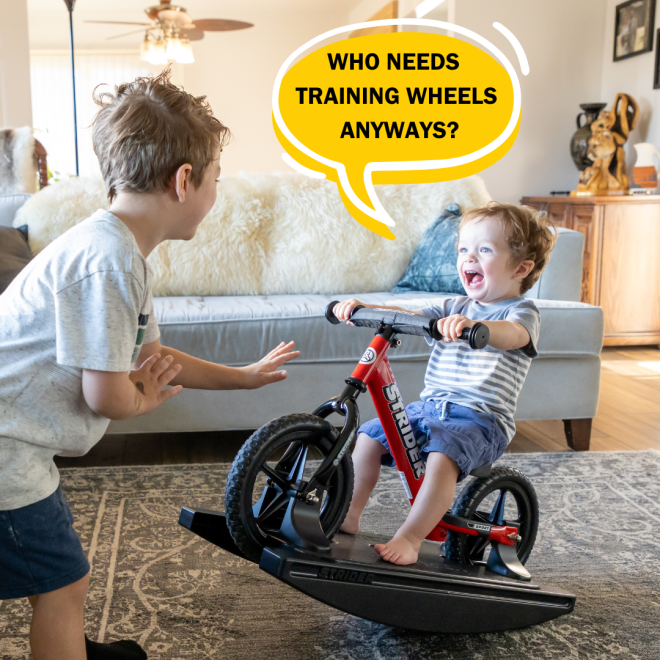 boys are playing in a living room. One is on a Strider 2-in-1 Rocking Bike with a huge smile. Why needs training wheels anyways?