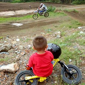 A child sits on their yellow Strider Bike while watching a motocross rider