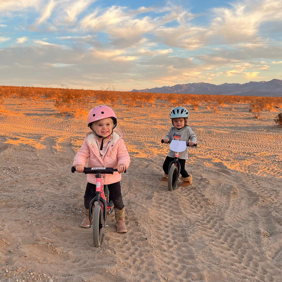Children happily ride through the dirt on a Pink and Orange Strider Sport Bikes.