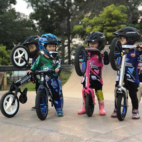 Toddlers in racing gear do wheelies with Strider bikes