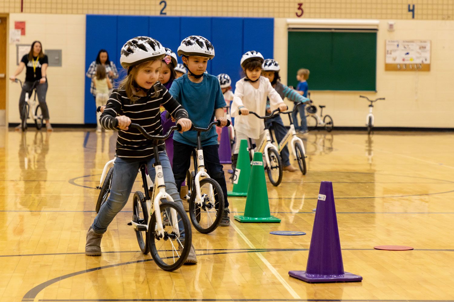 A group of kindergarteners bike around cones in a gym