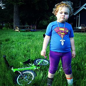 Girl stands in grass while looking unimpressed with her Strider Bike laying behind her