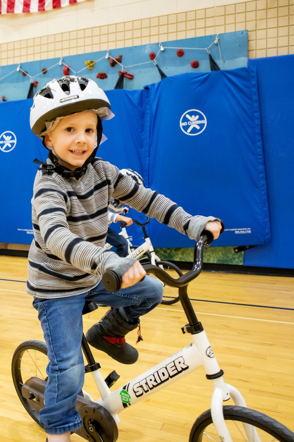 A boy smiles on a white Strider bike during the All Kids Bike curriculum