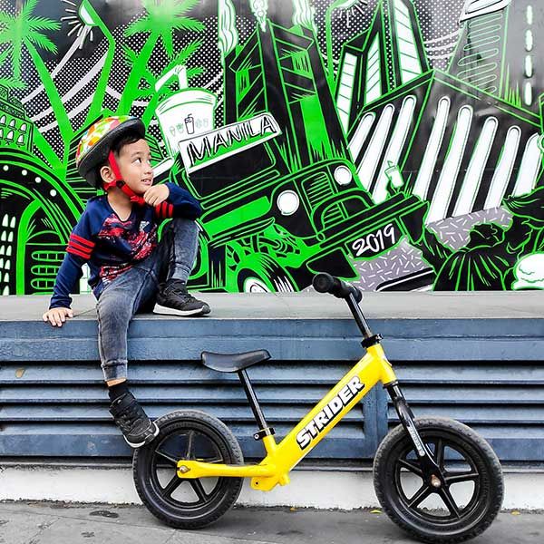 child and yellow bike in front of a mural
