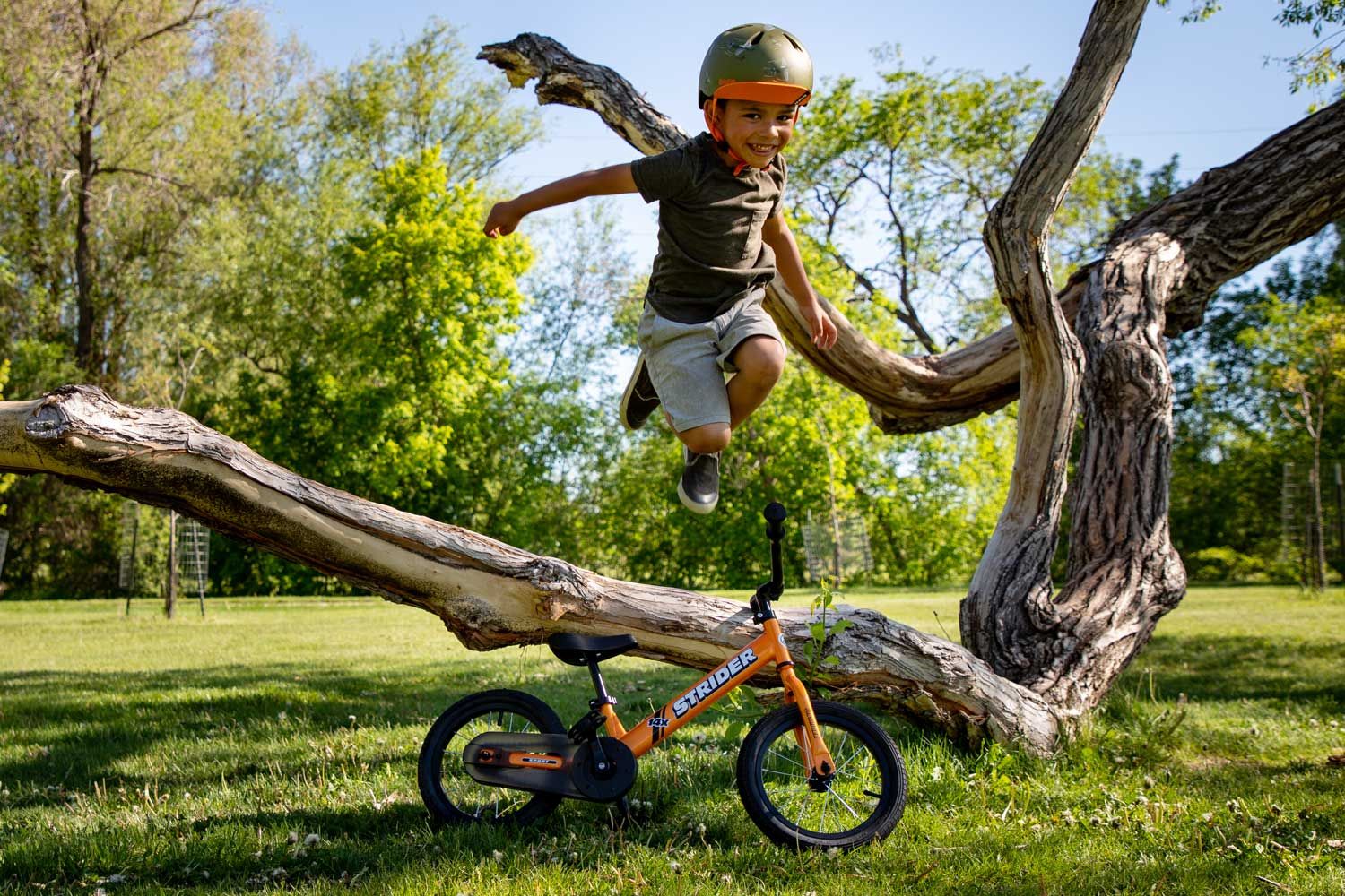 A child jumping over an orange Strider 14x pedal bike