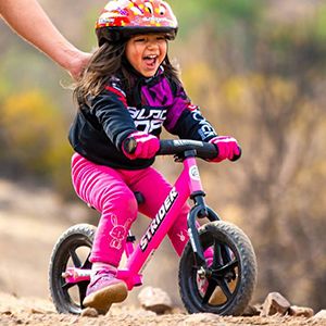 A child smiles with excitement while gliding on their pink Strider Bike