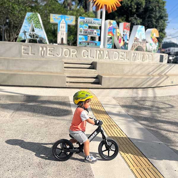Child rides Strider bike in front of Atenas sign in Costa Rica