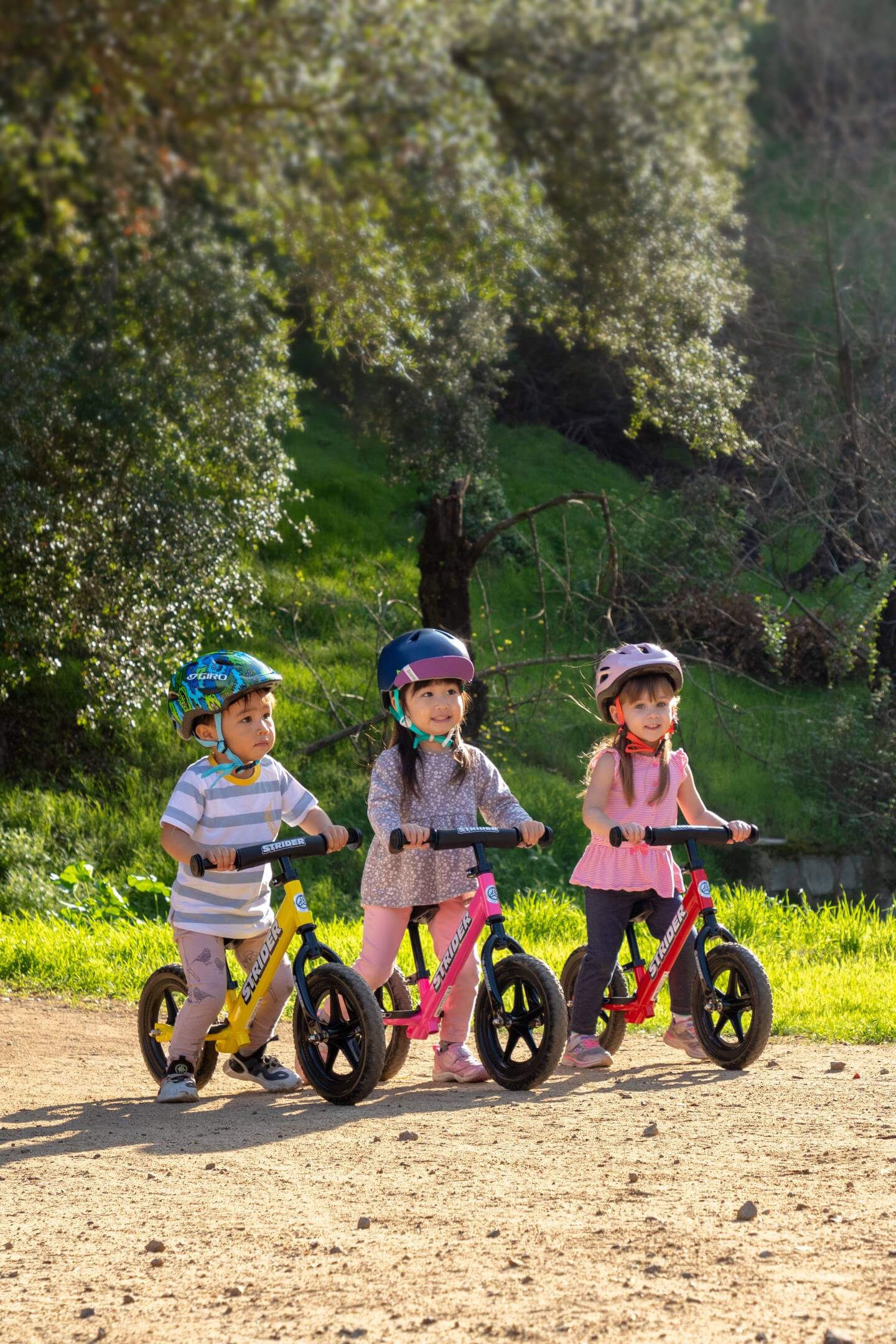 Three children on 12 inch Strider bikes ride on a dirt nature trail