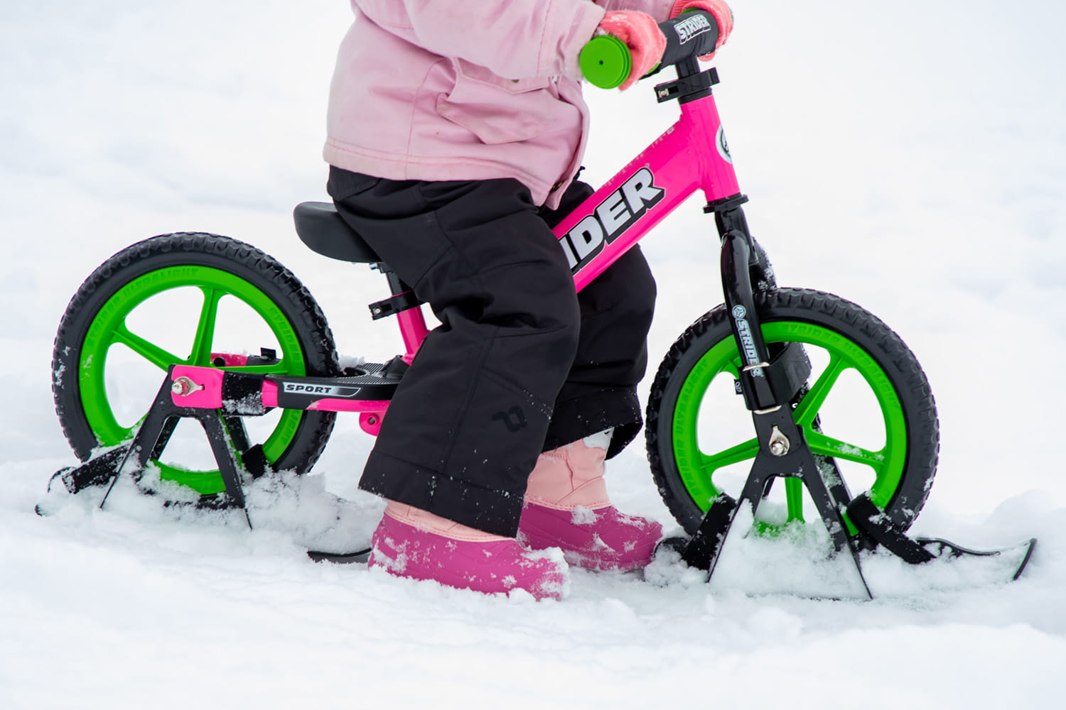 A closeup of Strider Snow Skis in use on a pink bike
