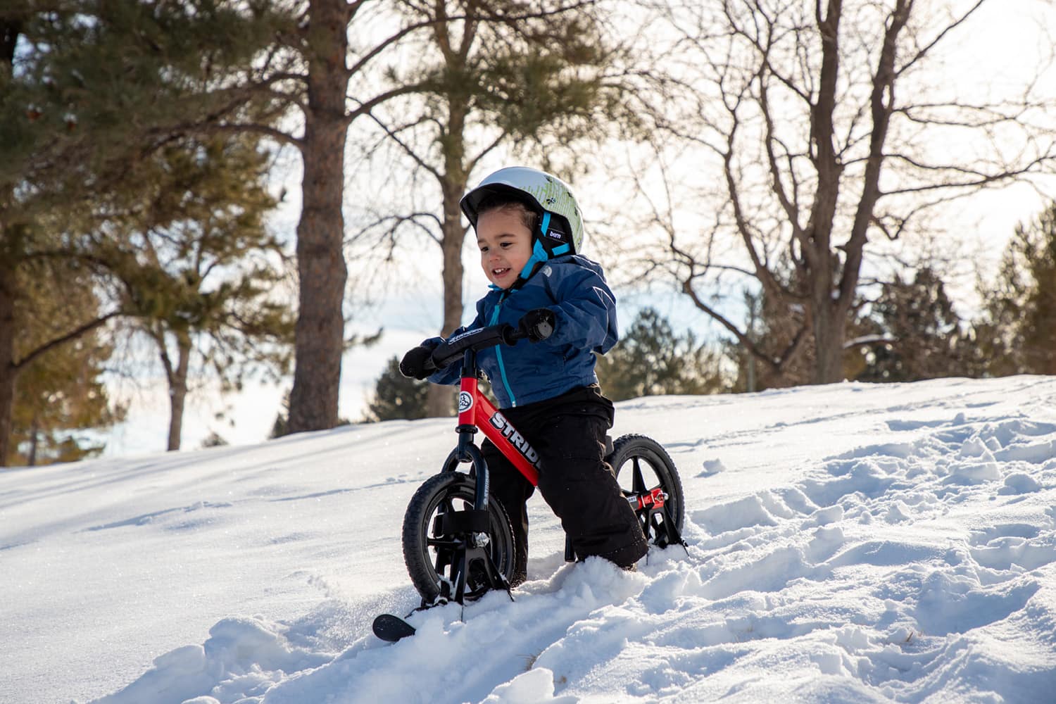 A boy on a red Strider bike skis down a snowy hill
