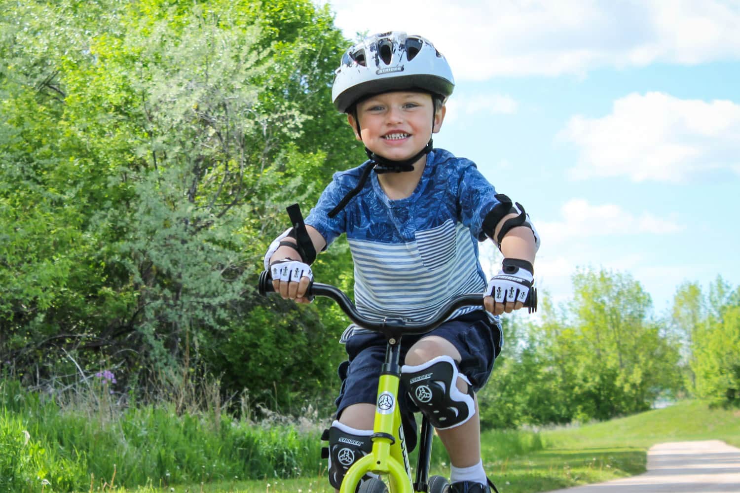 Smiling boy rides a bike with a Strider Splash helmet on