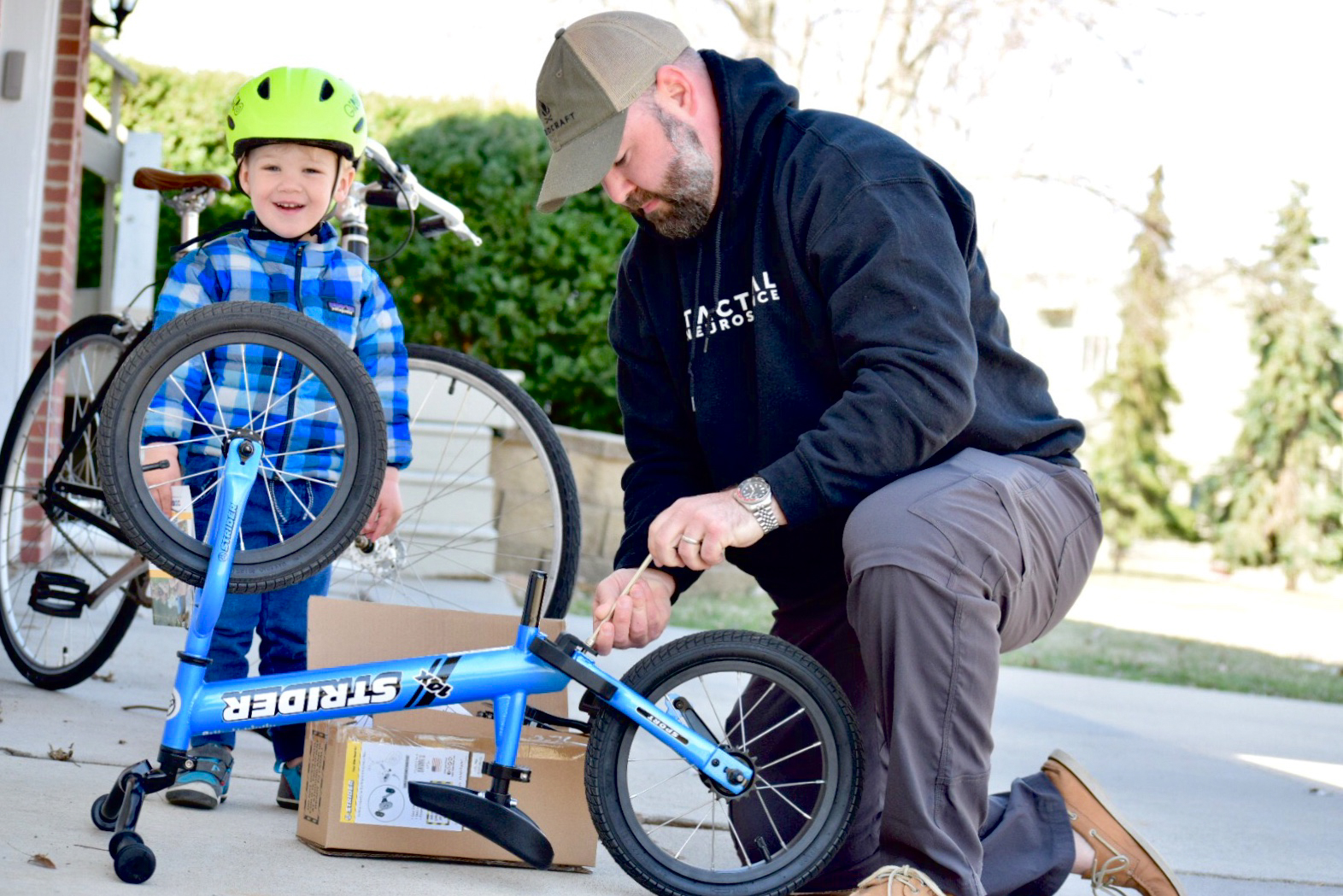 Dad helping attach Easy-Ride Pedal Kit to Strider 14x Sport blue bike with kid watching