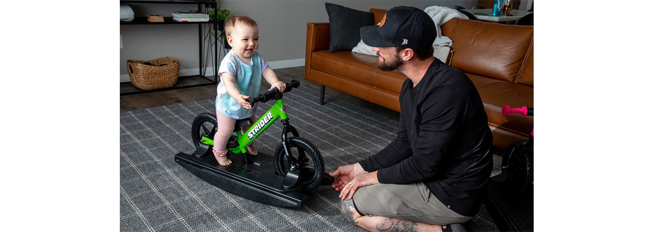 A baby on a green Rocking Bike laughs with Dad