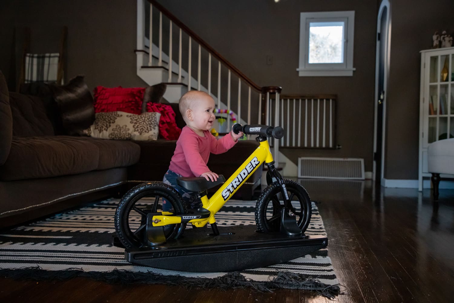 A baby plays alongside a yellow Strider Sport Rocking Bike