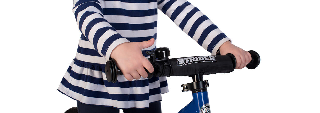 A child in a striped shirt rings the Strider Handlebar Bell