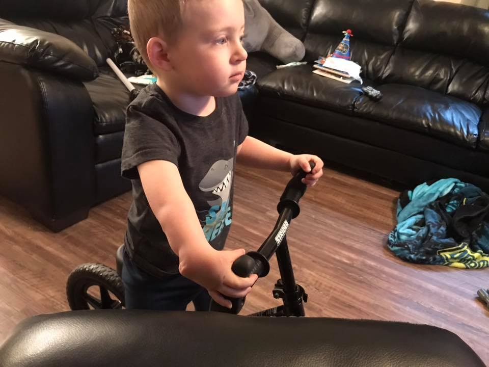Caden Mollohan with right radial aplasia stands on his adaptive 12" Strider Classic bike