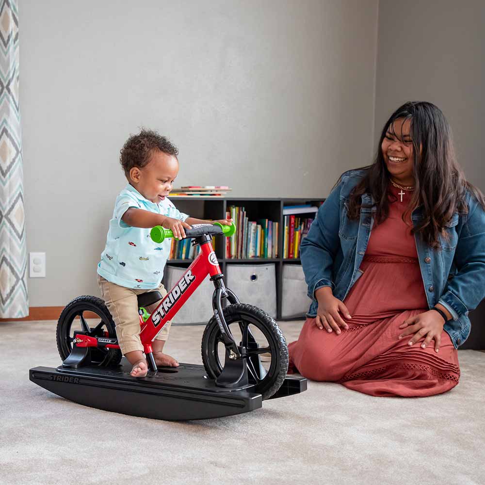 Baby and mom play with a red Strider Sport Rocking Bike